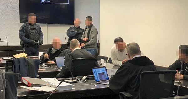 Die beiden Angeklagten G. und I. betreten in Begleitung von Justizbeamten den Gerichtssaal, K. (rechts) kommt als freier Mann durch den Eingang.