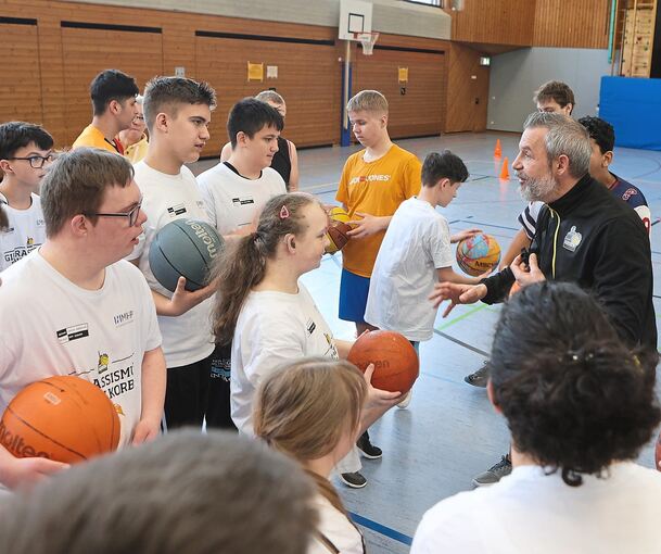 Marc Salzer, der Vereinskoordinator der MHP-Riesen, erklärt den Schülern das Dribbeln mit dem Basketball.
