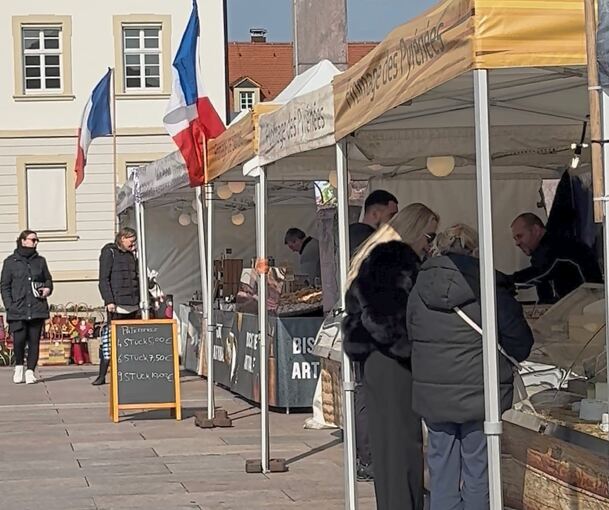 Besucher stöbern bei den Marktständen und genießen den französischen Markt bei Sonnenschein.