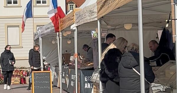 Besucher stöbern bei den Marktständen und genießen den französischen Markt bei Sonnenschein.