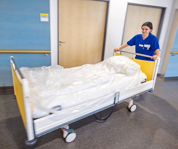 Eine junge Pflegerin schiebt ein Bett durch den Gang eines Altenheims.