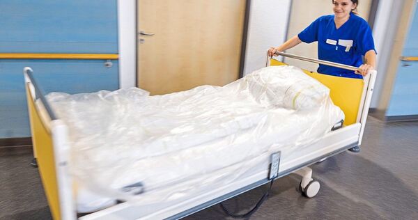 Eine junge Pflegerin schiebt ein Bett durch den Gang eines Altenheims.