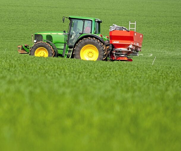 Ein Landwirt düngt mit Hilfe seines Treckers und eines Düngerstreuers sein Feld.