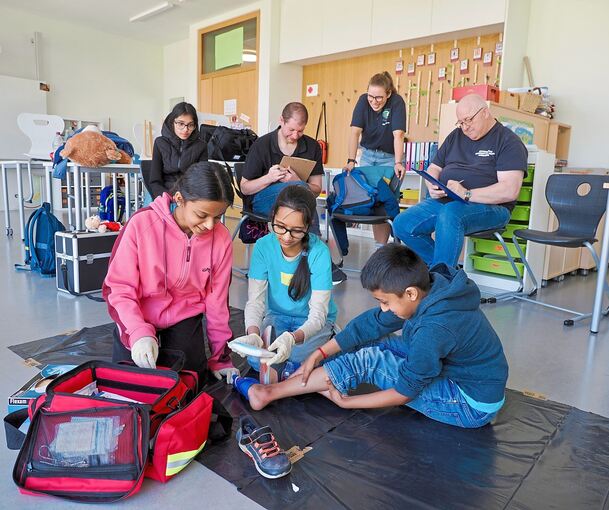 Die jungen Helferinnen und Helfer versorgen unter Beobachtung der Schiedsrichter eine Schürfwunde.