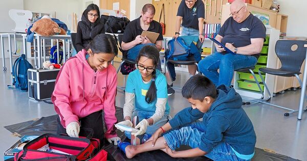 Die jungen Helferinnen und Helfer versorgen unter Beobachtung der Schiedsrichter eine Schürfwunde.