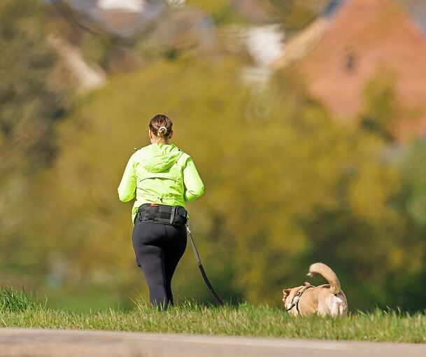Eine Joggerin ist mit ihrem Hund unterwegs.