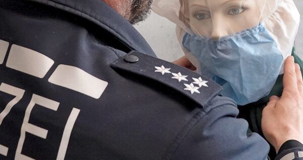 Ein Polizist demonstriert die Anwendung einer Spuckschutzhaube an einer Puppe.