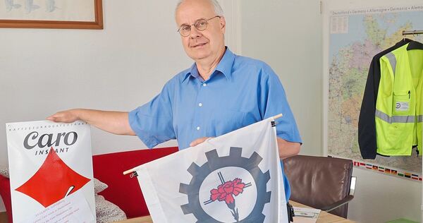 Christian Gojowczyk in seinem Büro in der Ludwigsburger Solitudestraße - mit dem Logo der Betriebsseelsorge (rechts), rote Nelke Christian Gojowczyk in seinem Büro in der Ludwigsburger Solitudestraße - mit dem Logo der Betriebsseelsorge (rechts), rote Nelken auf einem Kreuz in einem Zahnrad. Links: Ein Schild, das auf die Caro-Kaffee-Produktion in Ludwigsburg hinweist. Nestlé,