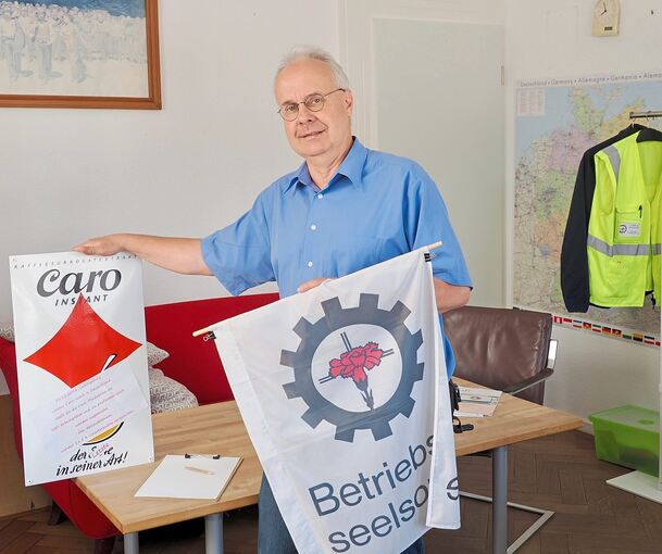 Christian Gojowczyk in seinem Büro in der Ludwigsburger Solitudestraße - mit dem Logo der Betriebsseelsorge (rechts), rote Nelken auf einem Kreuz in einem Zahnrad. Links: Ein Schild, das auf die Caro-Kaffee-Produktion in Ludwigsburg hinweist. Nestlé,