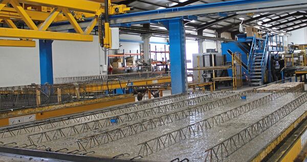 Eine Werkhalle mit Anlagen, auf denen Elementdecken hergestellt werden. Die Fertigung von Betonbauteilen im Werk unterscheidet sich zum Einsatz von Transportbeton, der auf die Baustelle transportiert und vor Ort verarbeitet wird.