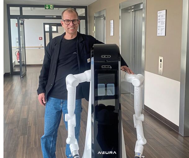 Felix Tirschmann mit einem Cobot. Das Design und wie er sich bewegt, passen gut in ein Patientenzimmer. Von der Seite kann man durchschauen, das macht ihn fast filigran.