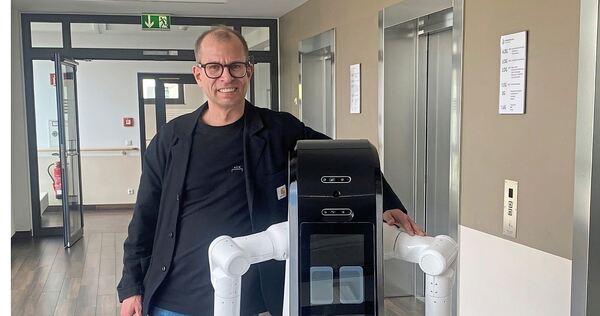 Felix Tirschmann mit einem Cobot. Das Design und wie er sich bewegt, passen gut in ein Patientenzimmer. Von der Seite kann man d Felix Tirschmann mit einem Cobot. Das Design und wie er sich bewegt, passen gut in ein Patientenzimmer. Von der Seite kann man durchschauen, das macht ihn fast filigran.