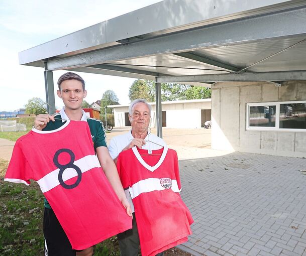 Uwe Düding (links) und Helmut Pistorius vom GSV-Förderverein hoffen auf einen hohen Erlös für die beiden Trikot-Raritäten. Im Hintergrund sind das neue Hüttle (rechts) und links dahinter das Materiallager zu sehen.