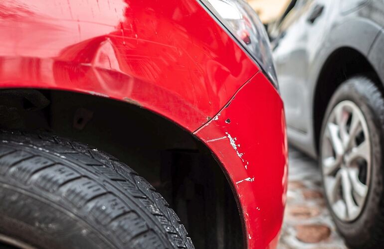 Das rote Auto steht mit einem Blechschaden in einer Parklücke, während ein graues Auto vorbeifährt. Die Regionalklasse bildet die Schadensbilanz eines Zulassungsbezirks ab.