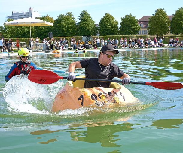 Viele Menschen haben zugeschaut, als Männer und Frauen in Riesenkürbissen über den See gepaddelt sind. Viele Menschen haben zugeschaut, als Männer und Frauen in Riesenkürbissen über den See gepaddelt sind.
