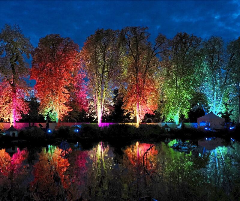 Die bunt beleuchteten Bäume spiegeln sich im See.