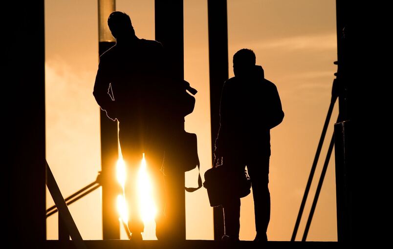 Zwei Männer gehen mit Aktentasche bei Sonnenaufgang über Brücke Zwei Männer gehen mit Aktentasche bei Sonnenaufgang über Brücke