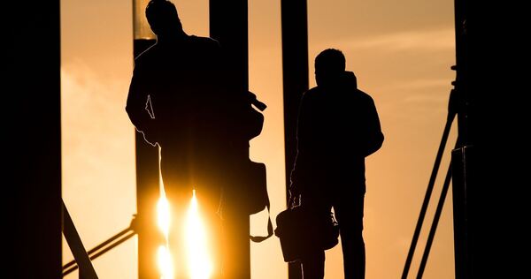 Zwei Männer gehen mit Aktentasche bei Sonnenaufgang über Brücke Zwei Männer gehen mit Aktentasche bei Sonnenaufgang über Brücke